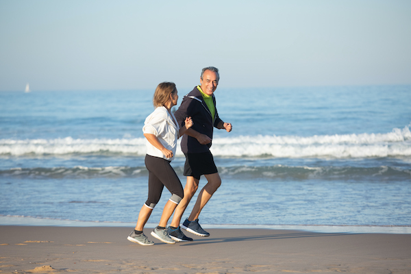 Ällteres Pärchen joggt lächend gemeinsam am Strand